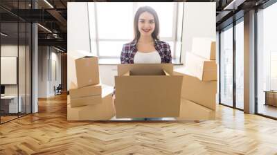 Young happy woman carrying a pile of cardboard boxes in her new hause, she is smiling at camera Wall mural